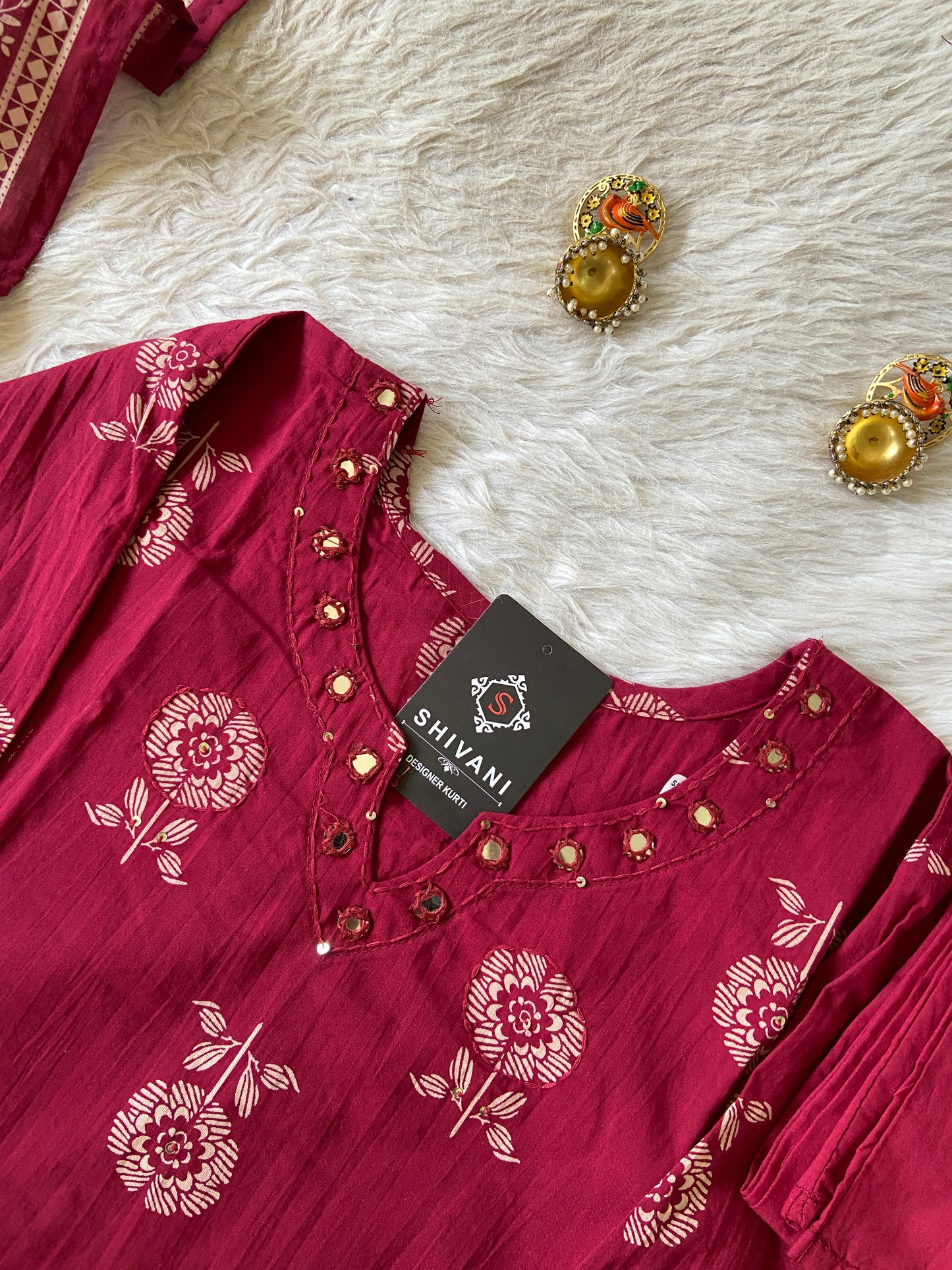Red floral-patterned shirt with a 'Shivani' tag on a textured white surface.