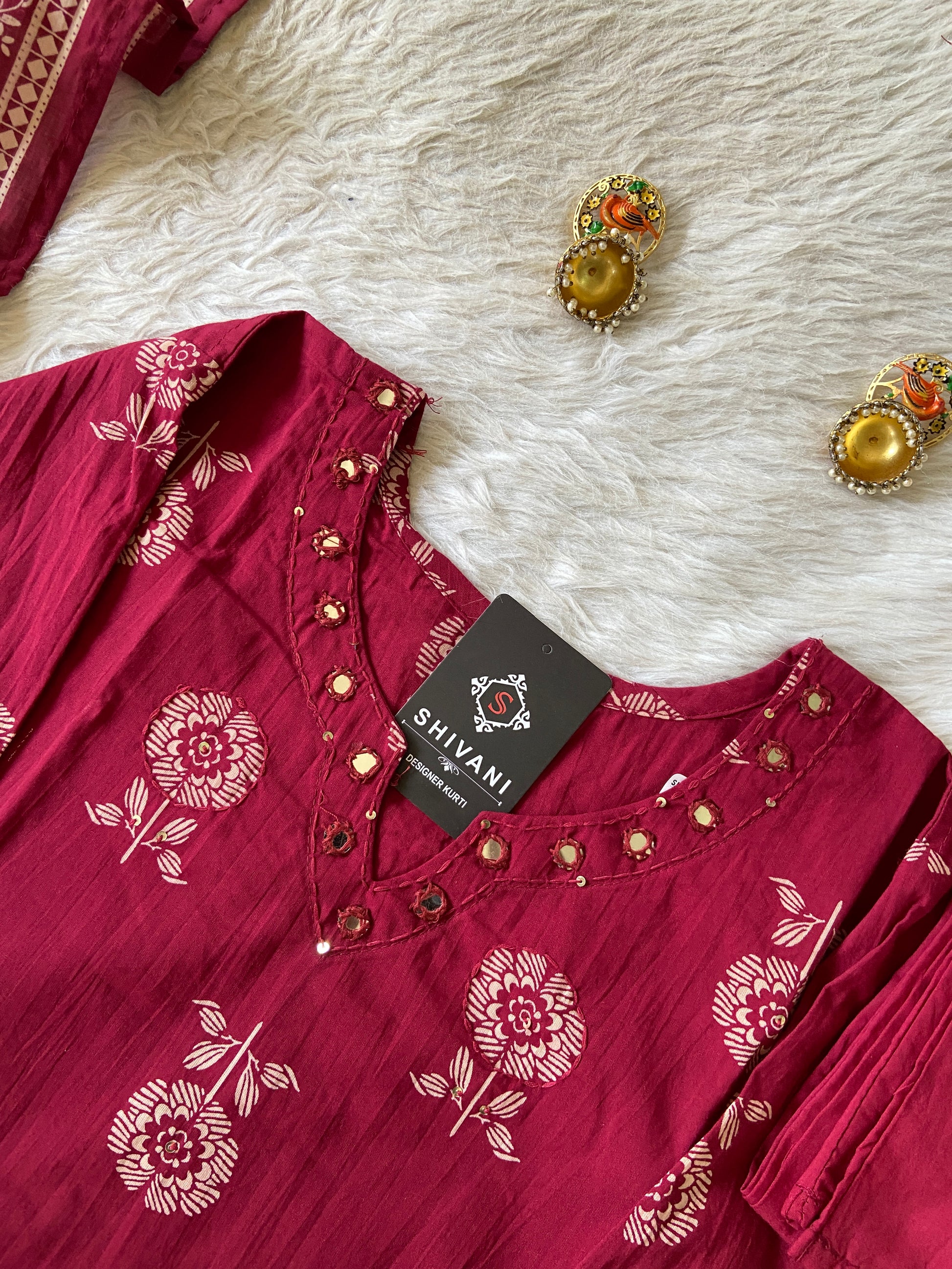 Red floral-patterned shirt with a 'Shivani' tag on a textured white surface.
