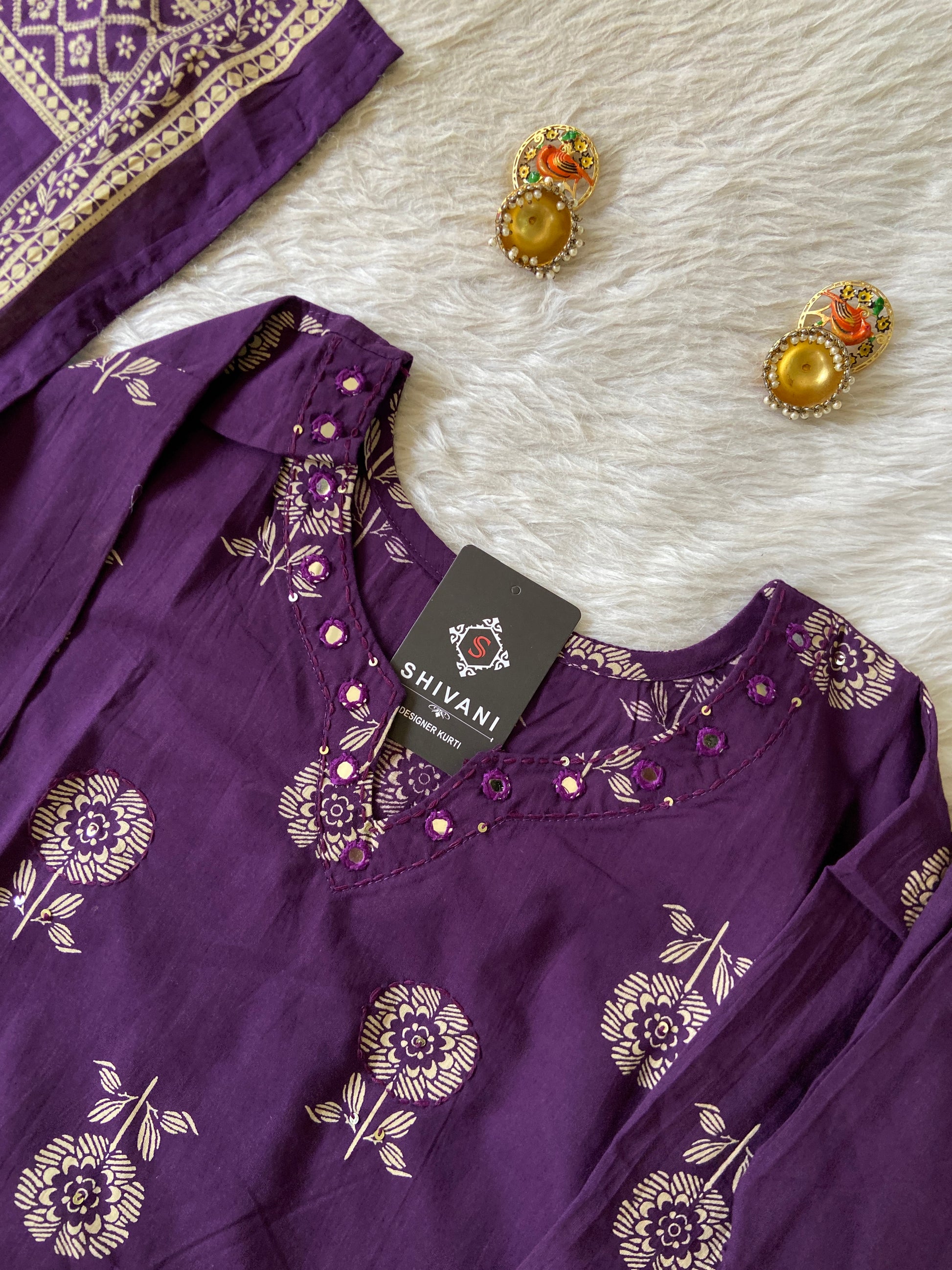 Purple embroidered garment with gold accents on a white fabric background