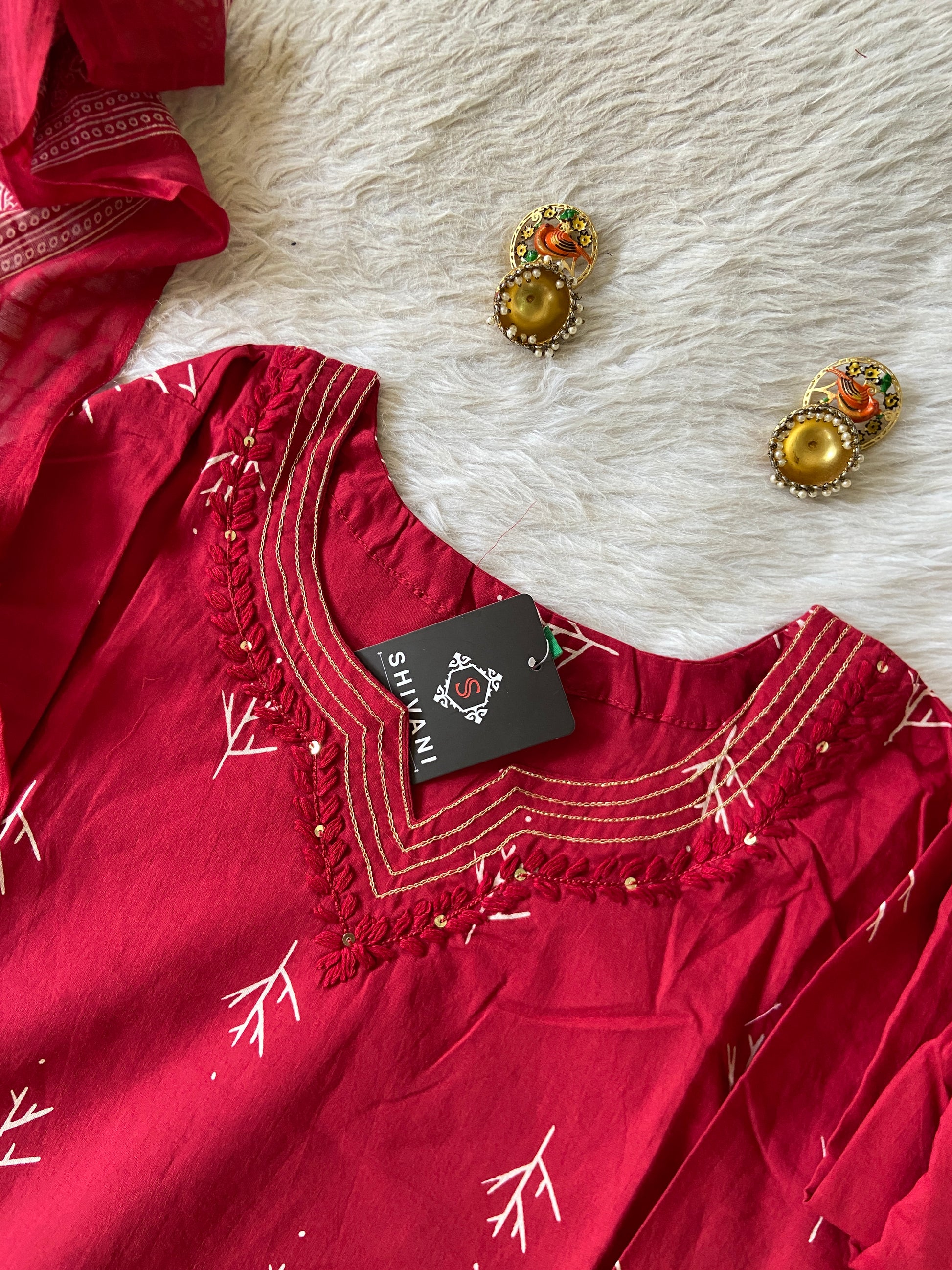 Red embroidered dress with gold detailing on a white fur surface, accompanied by matching earrings.