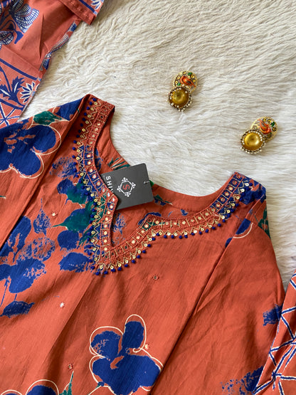 Orange floral dress with blue patterns on a white surface, accompanied by earrings.