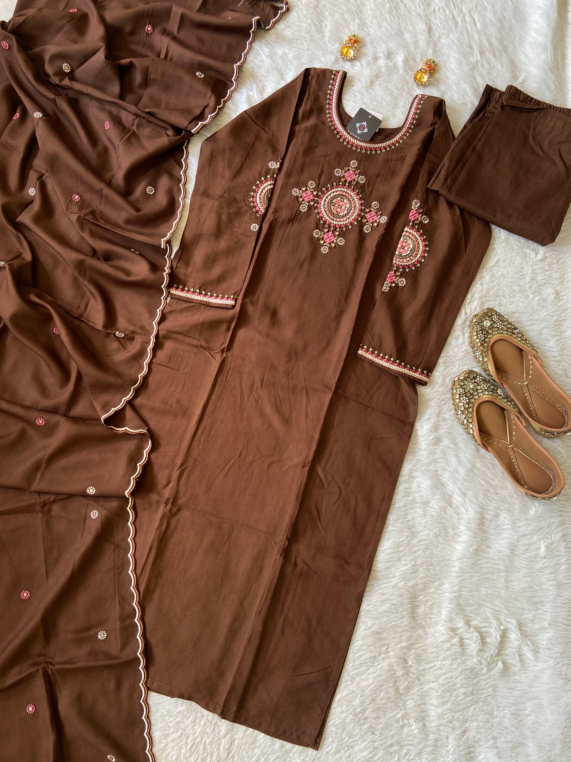Brown embroidered traditional outfit with gold shoes on a textured white surface