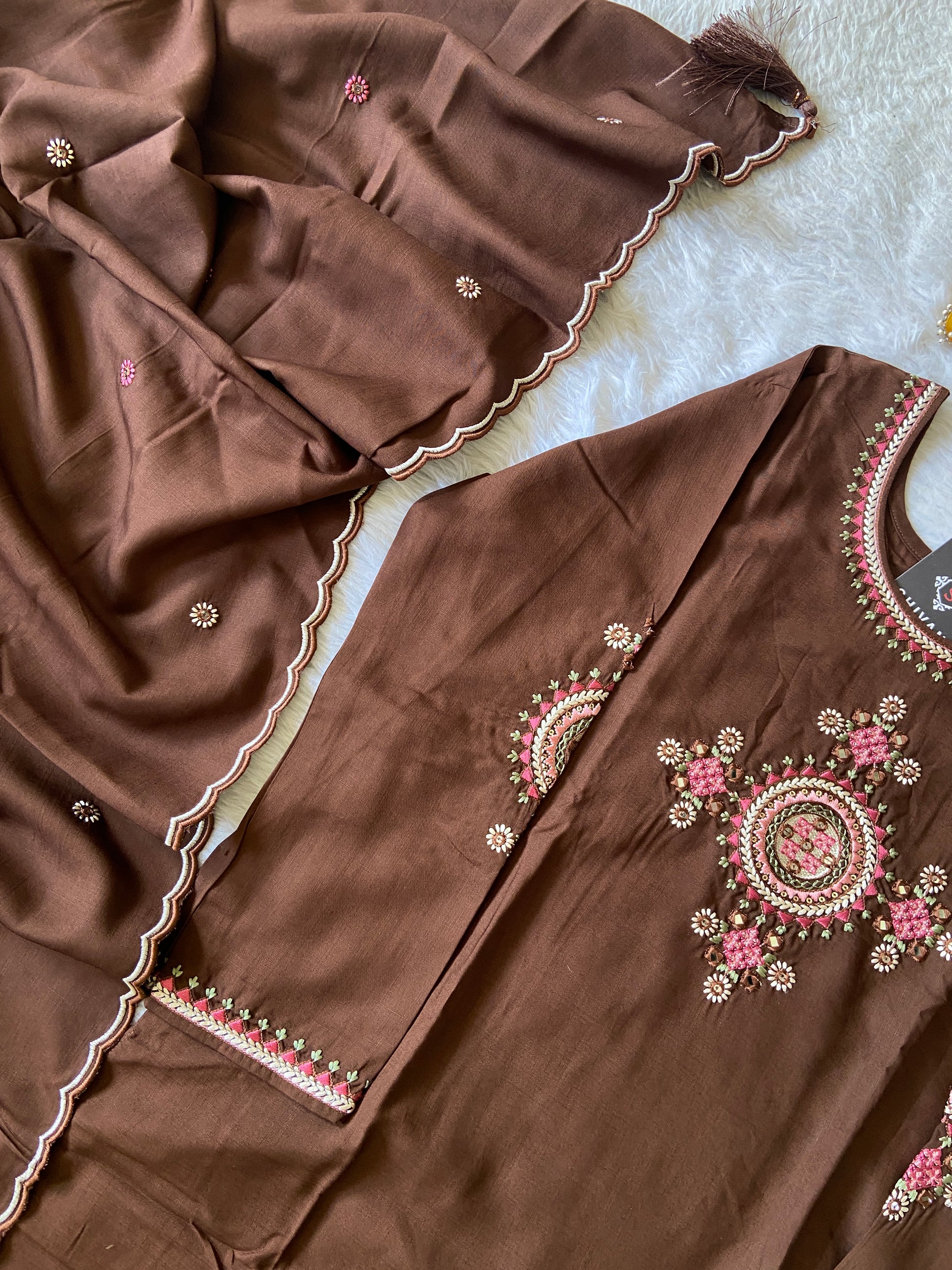 Brown fabric with intricate pink and gold embroidery on a textured surface