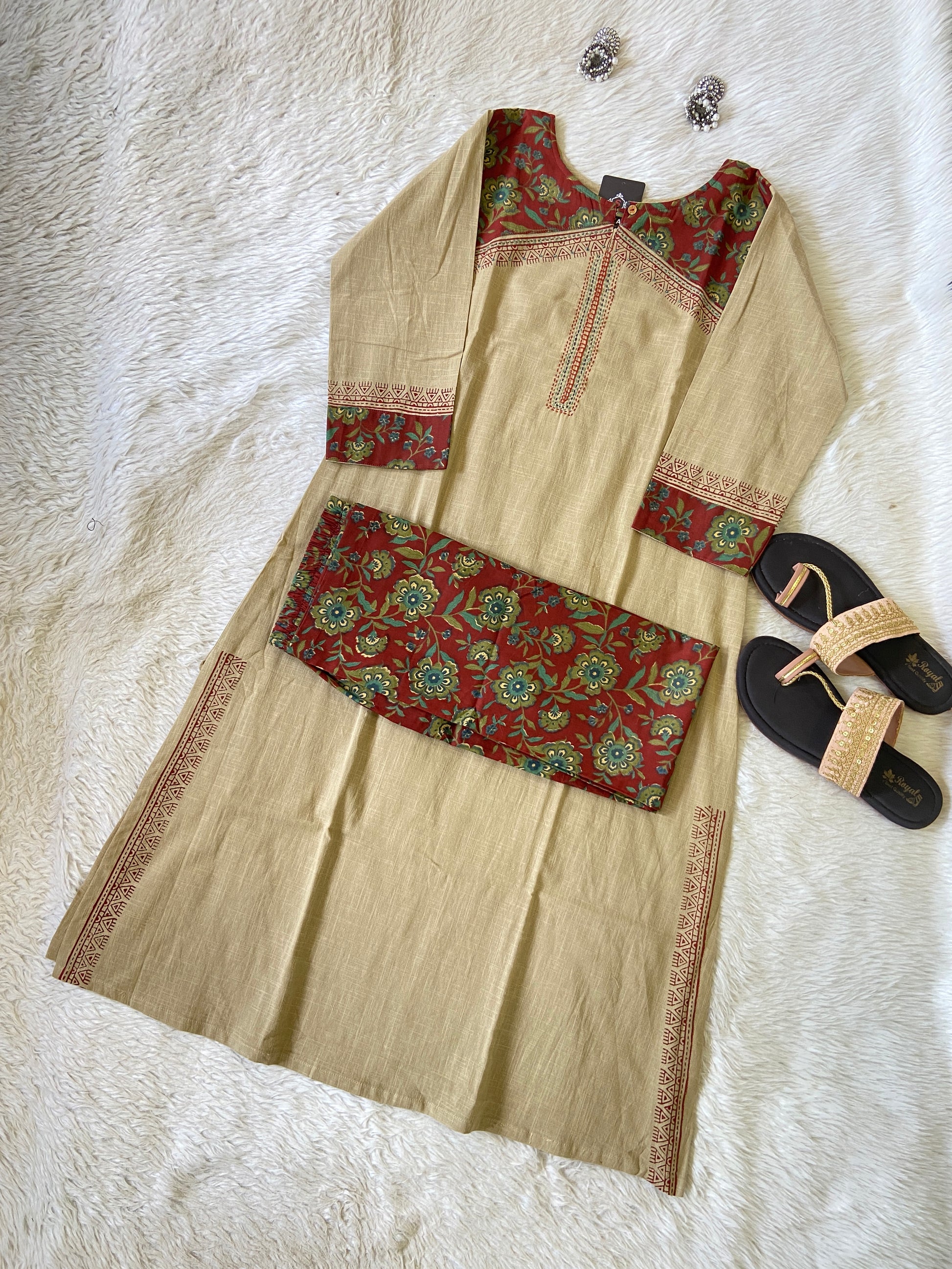 Beige traditional outfit with red and green patterns on a white textured surface